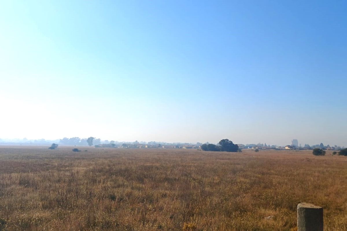 A wide-angle view of an expansive, undeveloped residential land plot with natural grass cover and distant horizon.
