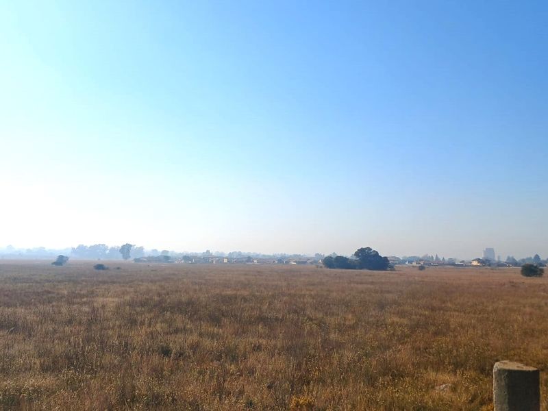 A wide-angle view of an expansive, undeveloped residential land plot with natural grass cover and distant horizon.