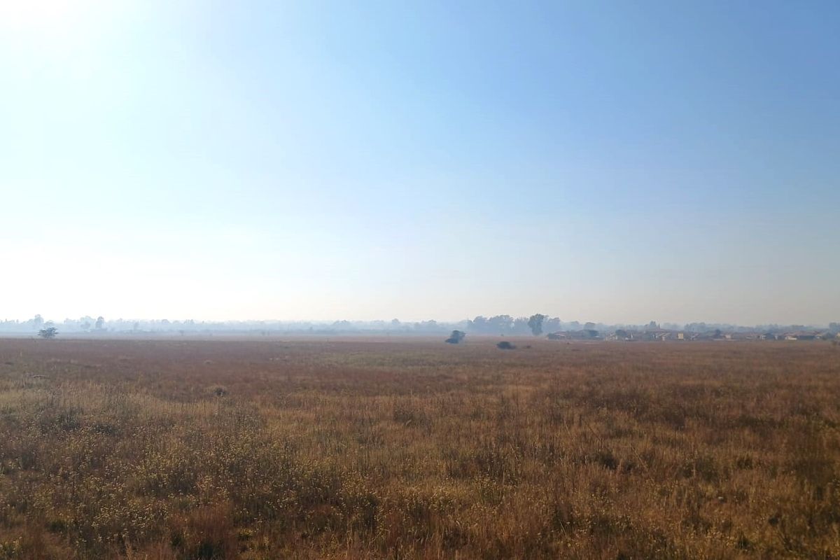 A wide, open expanse of vacant residential land featuring natural grassland under a clear sky.
