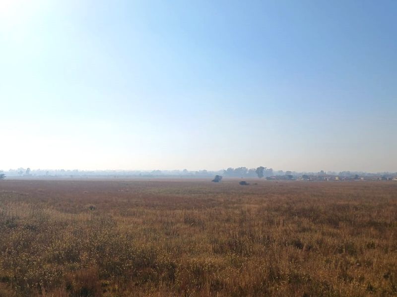 A wide, open expanse of vacant residential land featuring natural grassland under a clear sky.