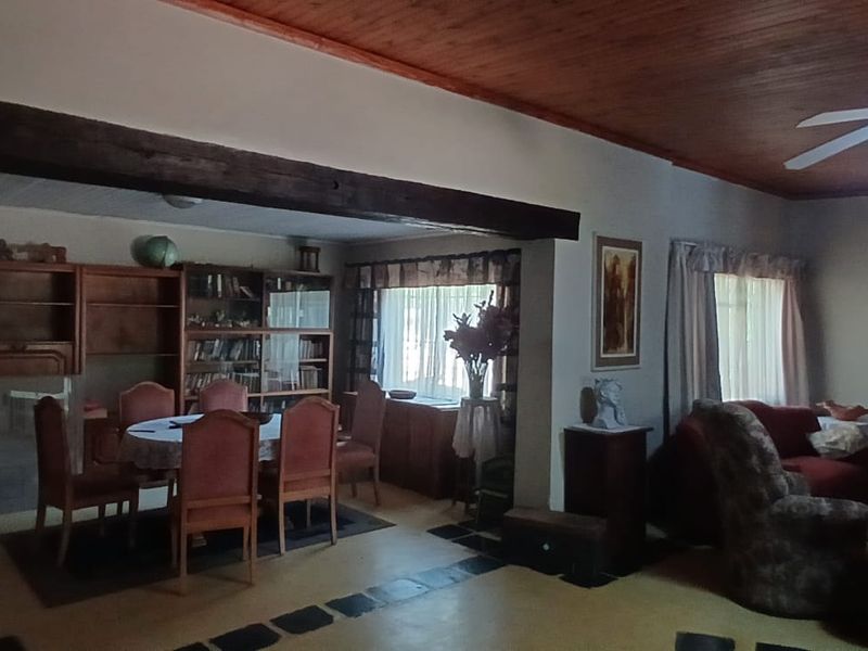 Spacious open-plan living and dining area featuring a timber-clad ceiling, exposed structural beam, and tiled flooring.