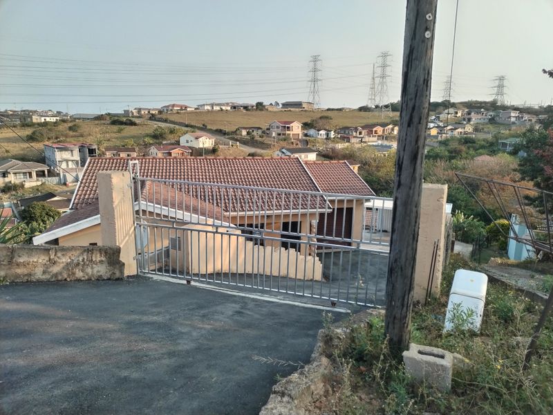 Elevated view of the property entrance featuring a metal security gate, paved driveway, and tiled roof structure overlooking the surrounding residential neighbourhood.