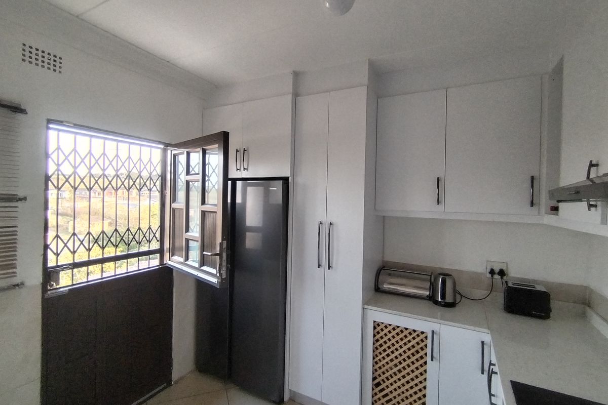 A functional kitchen featuring white cabinetry, stone-look countertops, and a security gate on the window, providing a clean and practical workspace.
