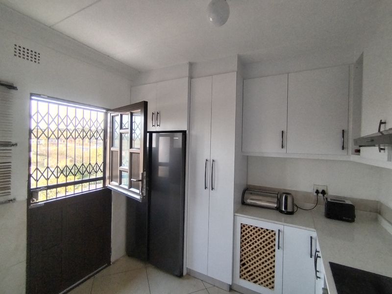 A functional kitchen featuring white cabinetry, stone-look countertops, and a security gate on the window, providing a clean and practical workspace.