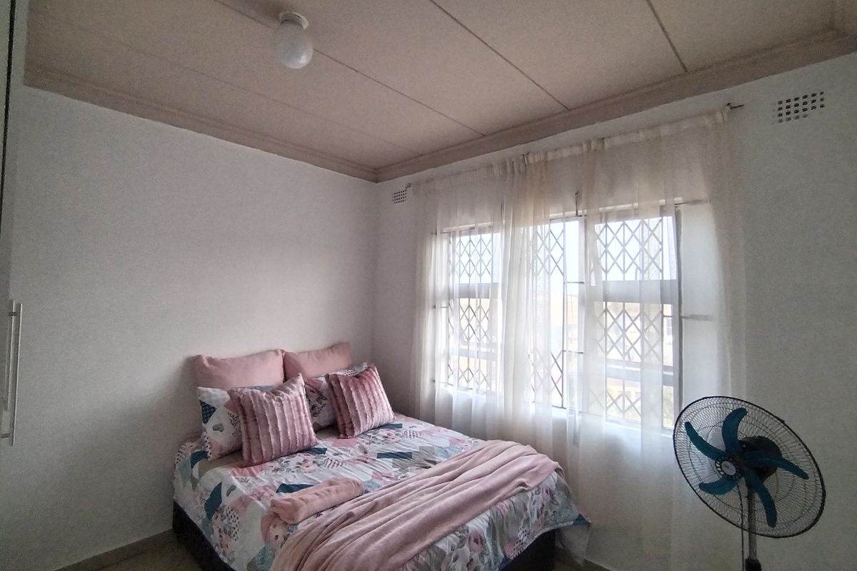 A functional bedroom featuring tiled flooring, security bars on the windows, and a simple ceiling finish.