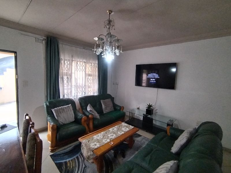 A living room featuring a central chandelier, tiled flooring, and security gates on the windows.