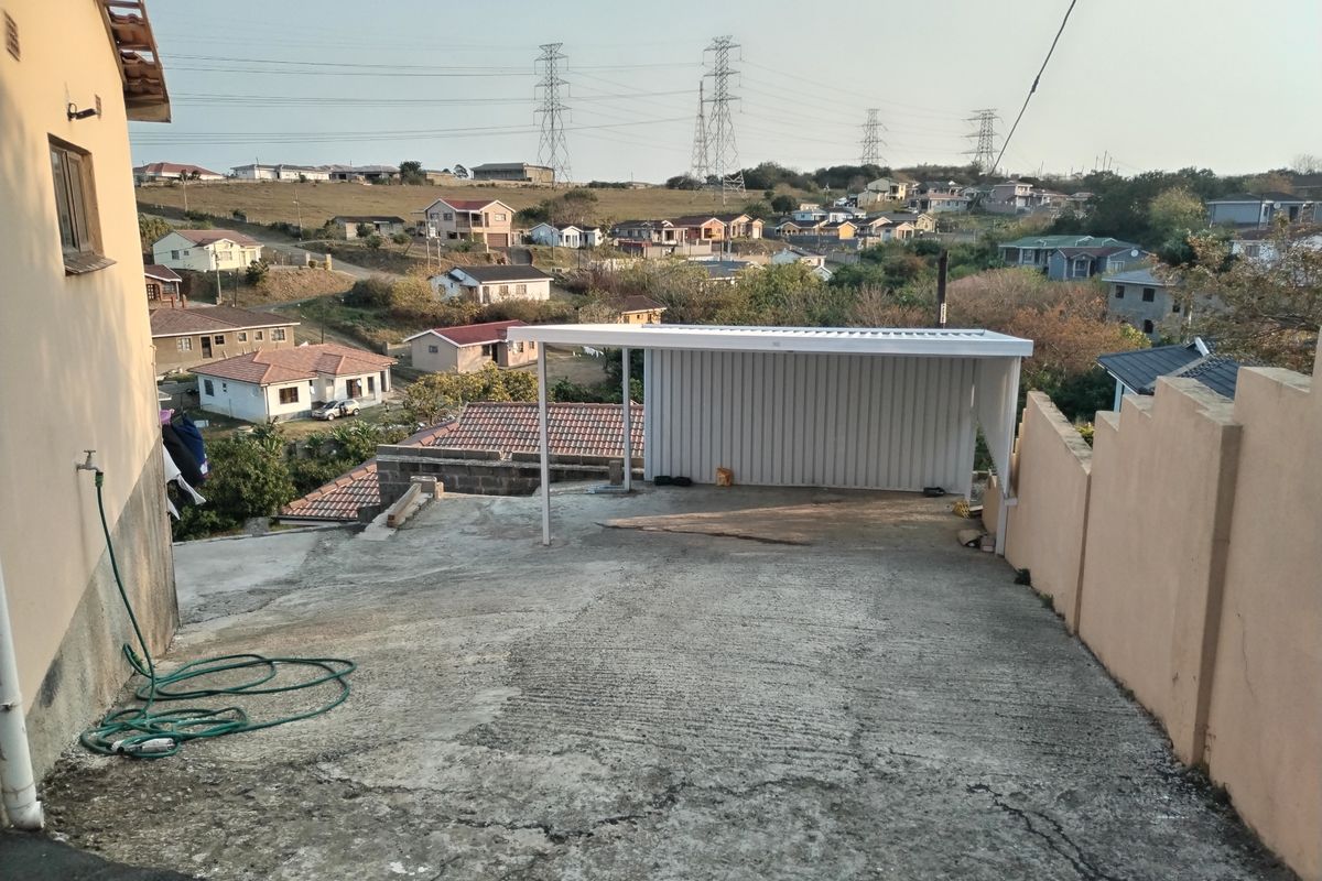 Exterior view of a concrete driveway featuring a metal carport structure, set against a residential neighbourhood backdrop.
