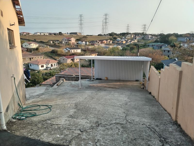 Exterior view of a concrete driveway featuring a metal carport structure, set against a residential neighbourhood backdrop.