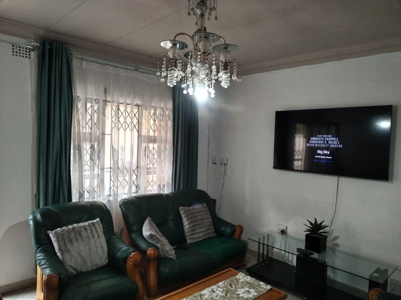 A living room featuring a decorative chandelier, security gate on the window, and wall-mounted television space.