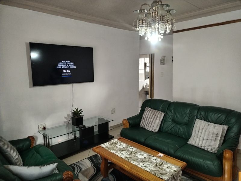 A living room featuring a central chandelier, tiled flooring, and a wall-mounted television setup.