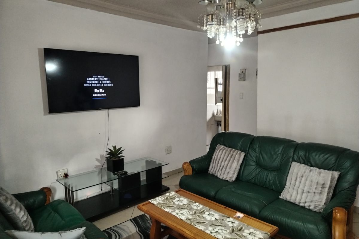 A living room featuring a central chandelier, tiled flooring, and a wall-mounted television setup.