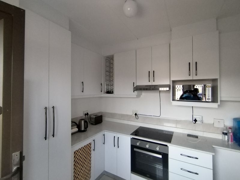 A clean, modern kitchen featuring white cabinetry, a built-in oven, electric cooktop, extractor fan, and integrated microwave space with ample counter workspace.
