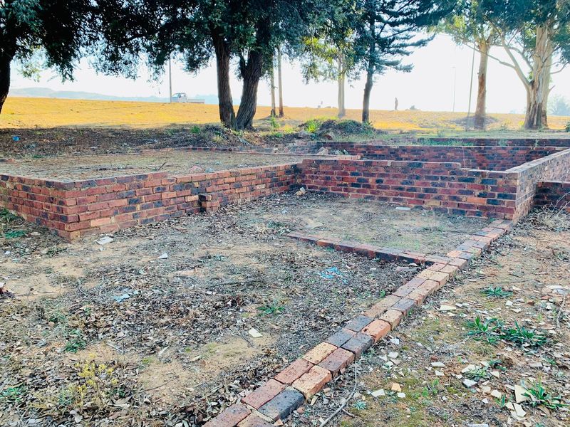 A vacant residential plot featuring partial brick foundation walls and established trees, offering a blank canvas for future development.