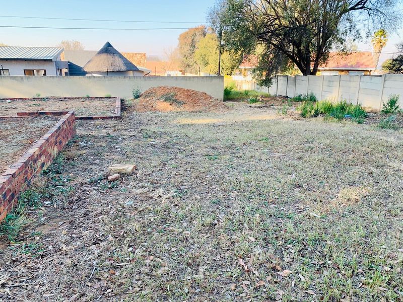 A vacant residential plot featuring a brick retaining wall and precast concrete boundary fencing, offering a blank canvas for landscaping or development.
