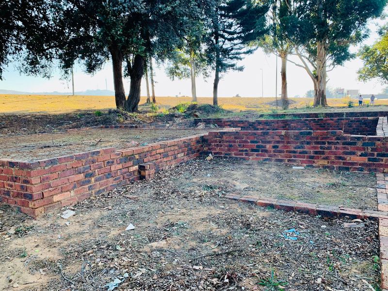 A vacant residential plot featuring partial brick foundation walls and mature trees, representing an early stage of construction or site preparation.
