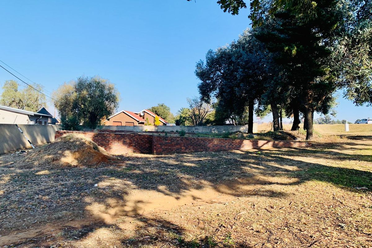 A vacant residential plot featuring a brick retaining wall, mature trees, and established boundary fencing, offering a clear space for future development.