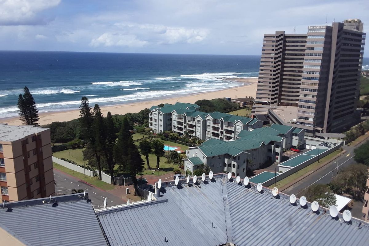 Elevated aerial view overlooking the coastline, beach, and surrounding residential apartment complexes.