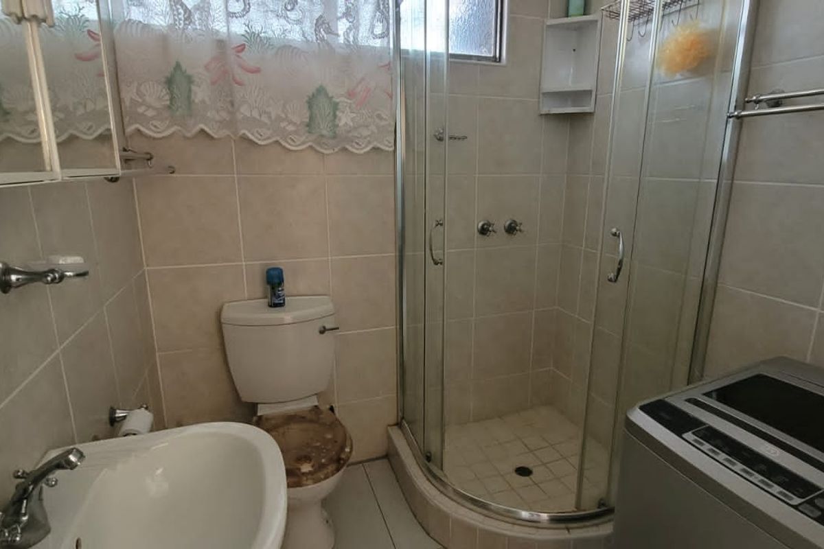 Compact bathroom featuring a corner shower enclosure, pedestal basin, and toilet, with tiled walls and flooring throughout.