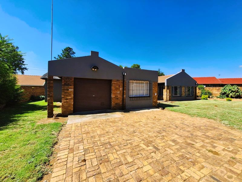 Front exterior view of the house featuring a brick driveway, single garage, and secure window bars set within a well-maintained garden.