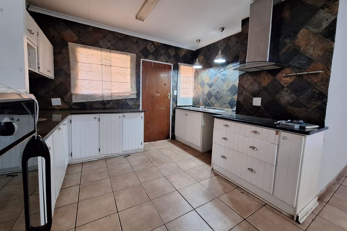 Functional kitchen featuring white cabinetry, dark stone tile backsplash, stainless steel extractor fan, and ceramic floor tiles.