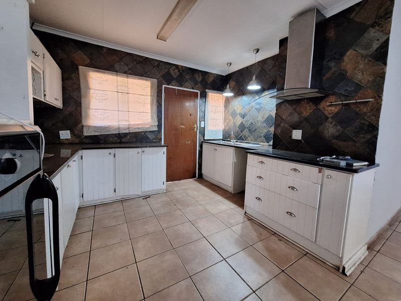 Functional kitchen featuring white cabinetry, dark stone tile backsplash, stainless steel extractor fan, and ceramic floor tiles.