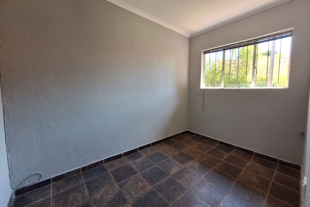 A clean, empty bedroom featuring dark tiled flooring, textured grey walls, and a window fitted with security bars.