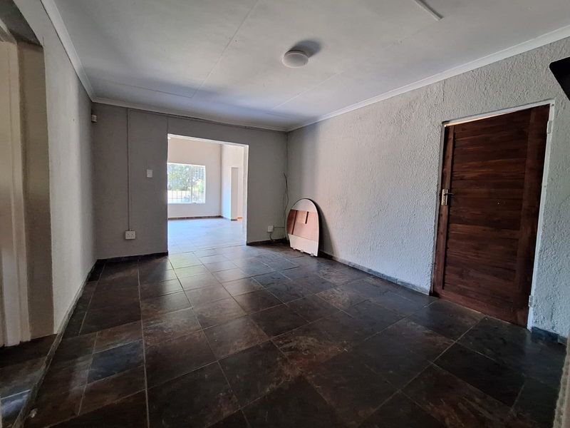 An empty living area featuring dark tiled flooring, a wooden door, and visible surface-mounted electrical conduit on the walls.