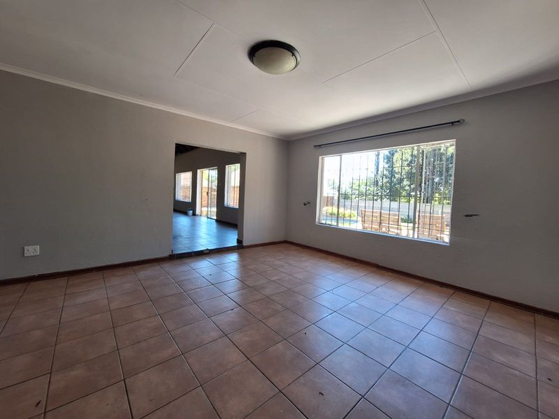 An empty living room featuring ceramic tile flooring, a large window with security bars, and neutral wall finishes, ready for personalization.
