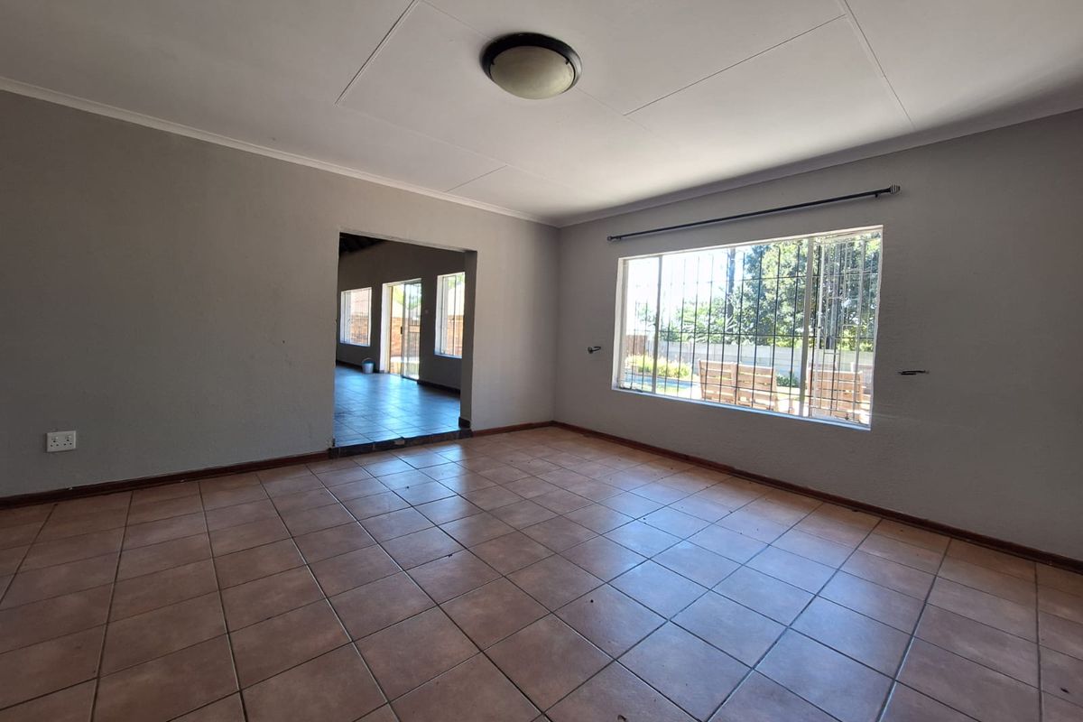 An empty living room featuring ceramic tile flooring, a large window with security bars, and neutral wall finishes, ready for personalization.