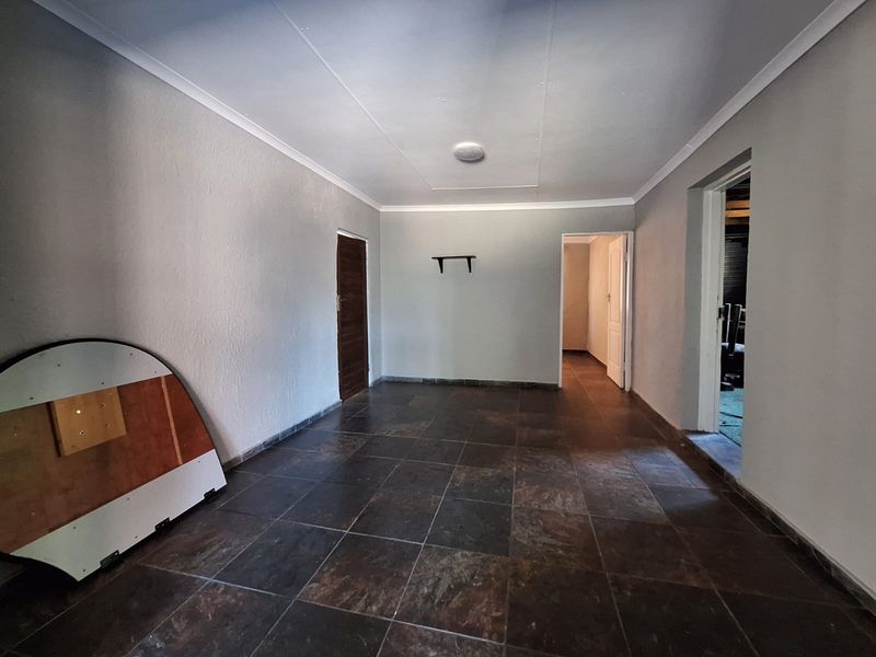 An empty living area featuring dark tiled flooring, neutral walls, and coved ceilings, providing a versatile space ready for personalization.