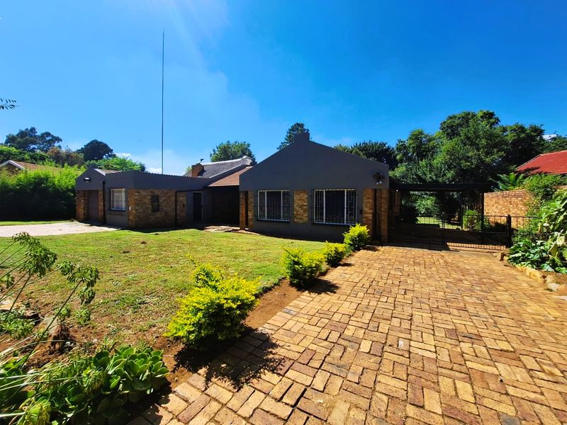 Front view of a single-story brick house featuring a paved driveway, carport, and established garden area.