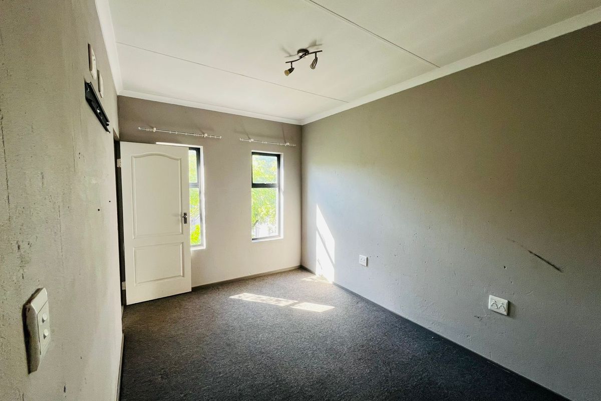 An empty bedroom featuring grey carpet flooring, neutral wall tones, and natural light from two windows.