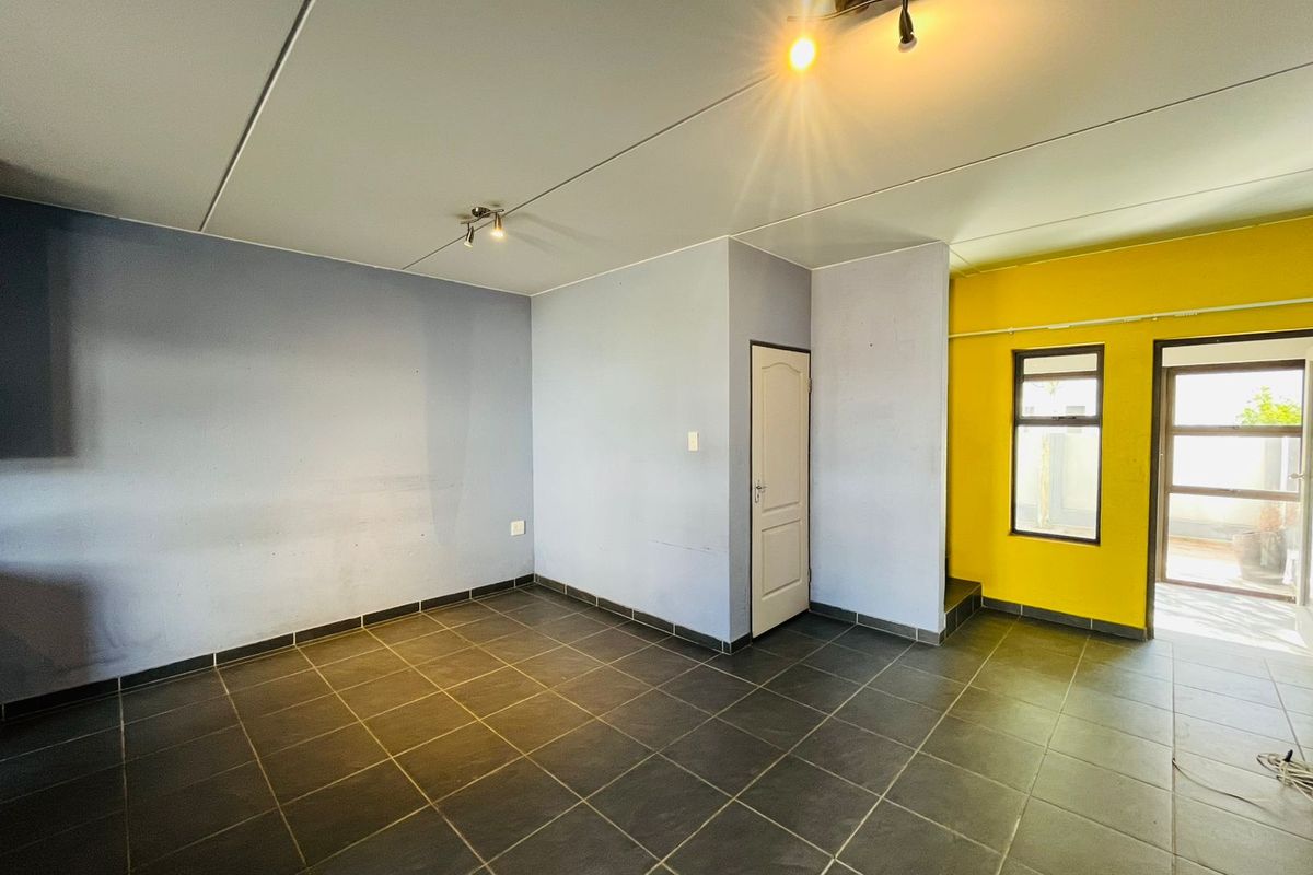 An empty living area featuring dark tiled flooring, neutral and yellow painted walls, and direct access to an outdoor space.