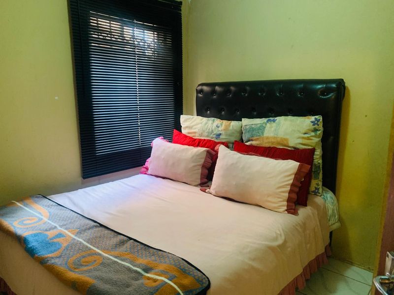 A compact bedroom featuring tiled flooring and dark venetian blinds. The space would benefit from a fresh coat of paint to improve its overall condition.