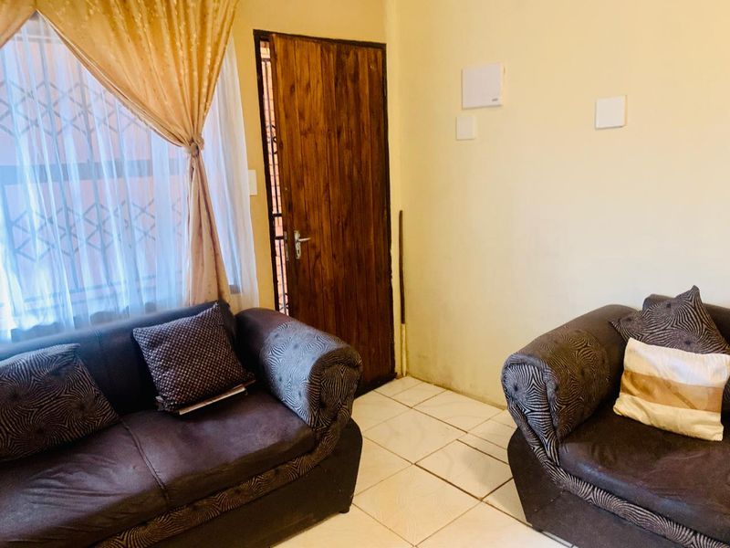 A living room area featuring tiled flooring, a wooden entrance door, and a security gate, showing signs of wear on the walls.