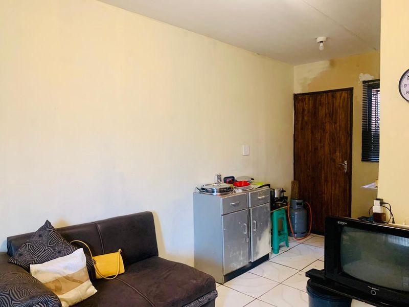 Open plan living area featuring tiled flooring and a wooden door, requiring cosmetic updates and wall repairs to improve the overall aesthetic.