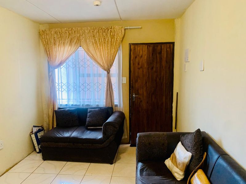 A living room featuring tiled flooring, a wooden door, and a window fitted with a security gate.