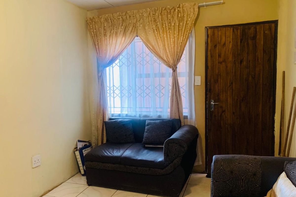 A living room area featuring tiled flooring, a wooden door, and a window fitted with a security gate.