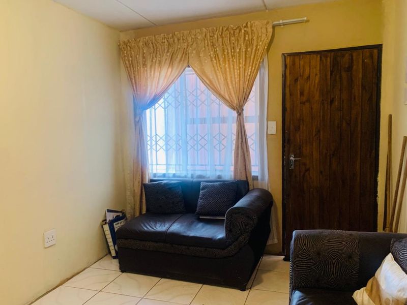 A living room area featuring tiled flooring, a wooden door, and a window fitted with a security gate.