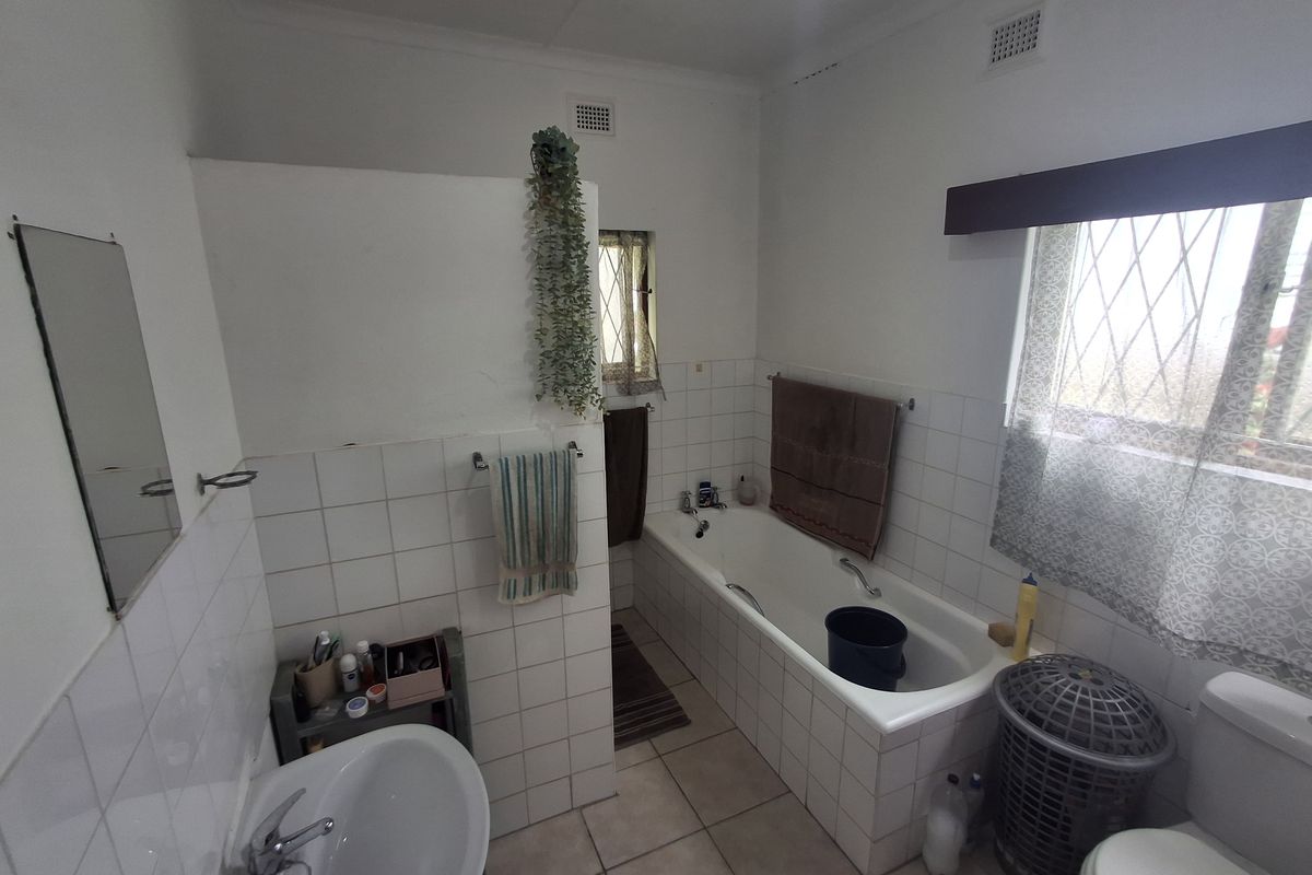 A functional bathroom featuring a built-in bathtub, pedestal basin, and toilet with tiled walls and flooring.