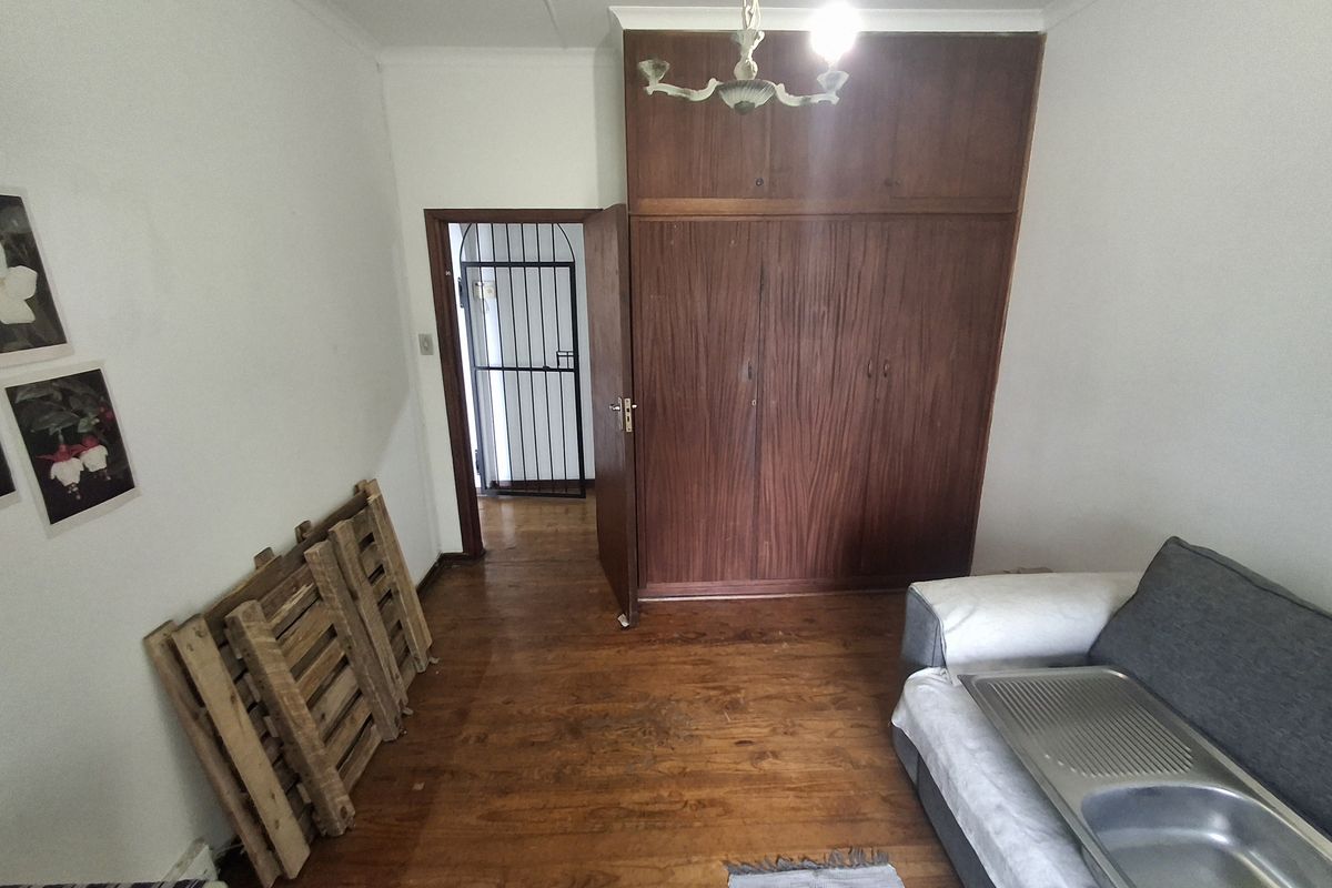 A bedroom featuring original timber flooring, built-in wooden cabinetry, and a security gate at the entrance.