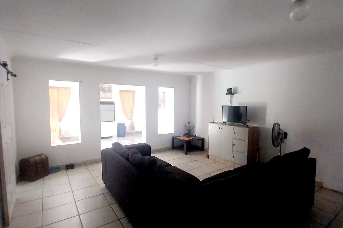 A spacious living room featuring neutral ceramic floor tiles and direct access to an adjacent room through large openings.