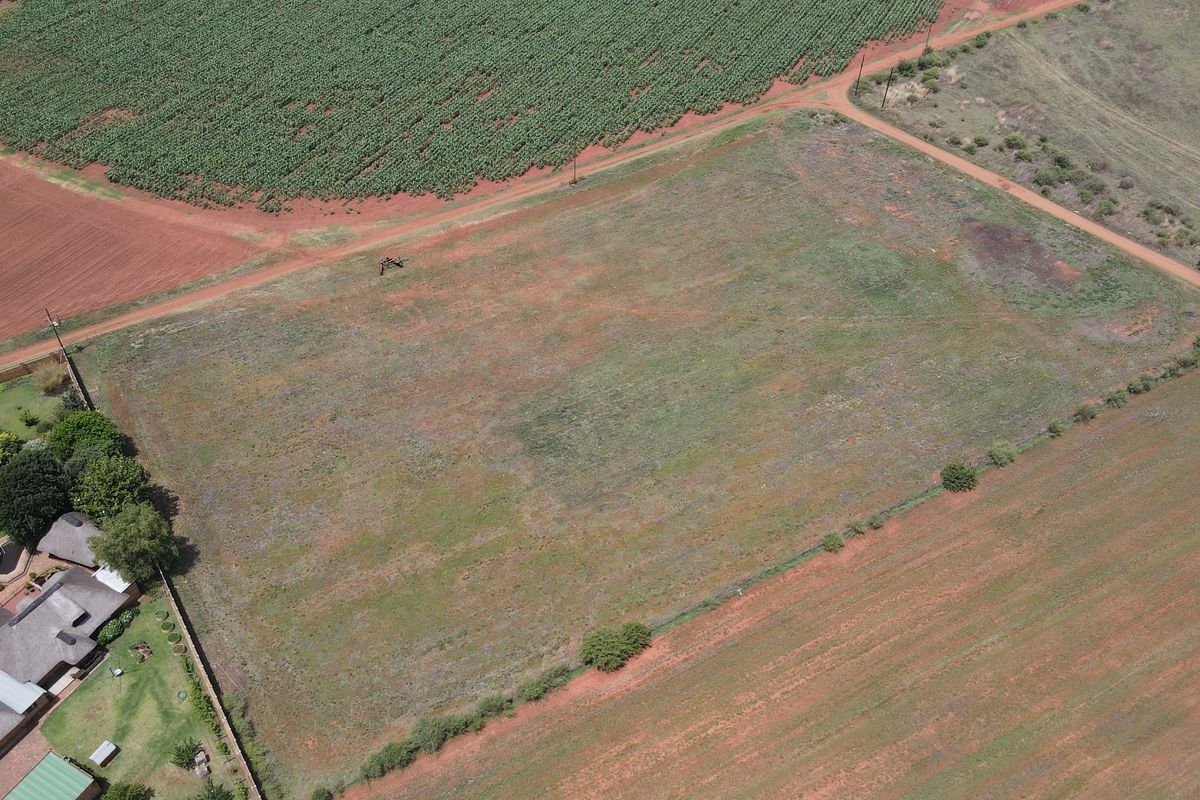 An aerial view of a vacant residential plot featuring open land, dirt access roads, and surrounding agricultural fields.