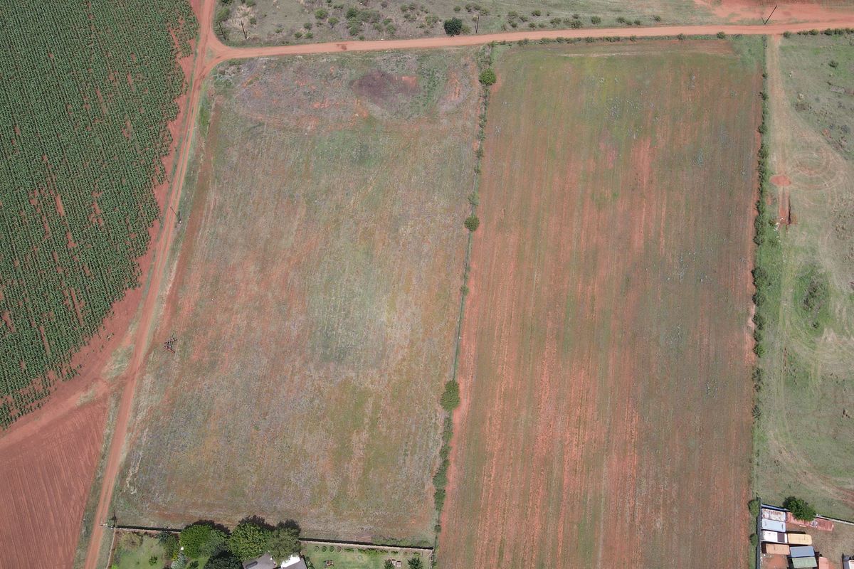Aerial view of a large, vacant residential land parcel with dirt road access and perimeter fencing.