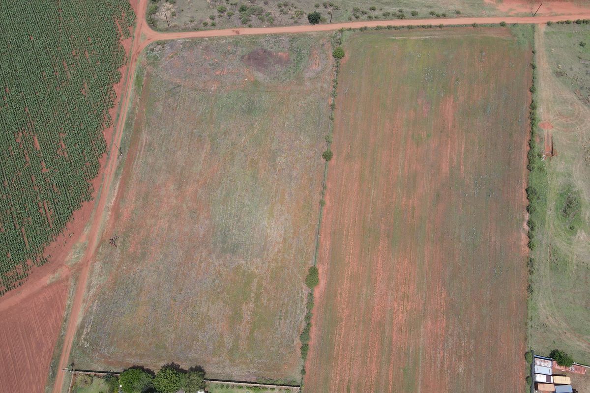 An aerial view of a vacant residential land plot featuring open terrain, perimeter fencing, and direct access to a dirt road.