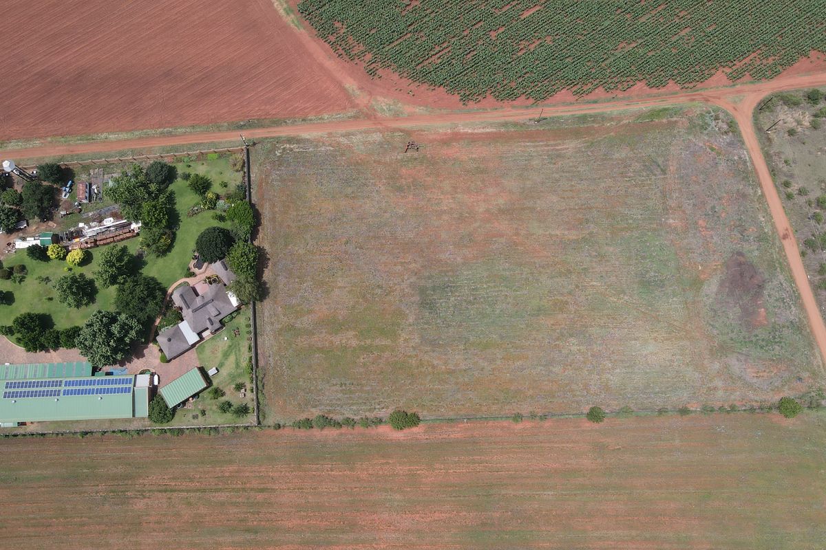 Aerial view of a large, vacant residential plot of land adjacent to an existing property with established garden and structures.