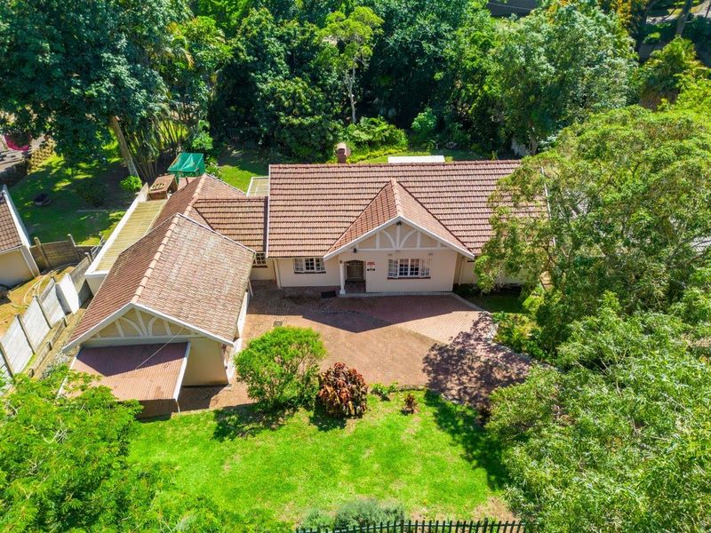 Aerial view of a residential property featuring a tiled roof, brick paved driveway, and established garden surroundings.