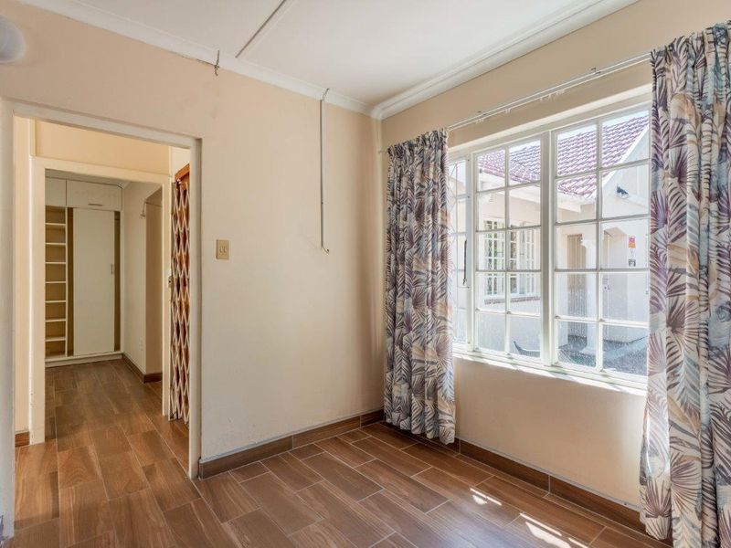 A vacant bedroom featuring tiled flooring, a multi-pane window, and built-in cupboard storage, requiring minor cosmetic repairs to the walls.