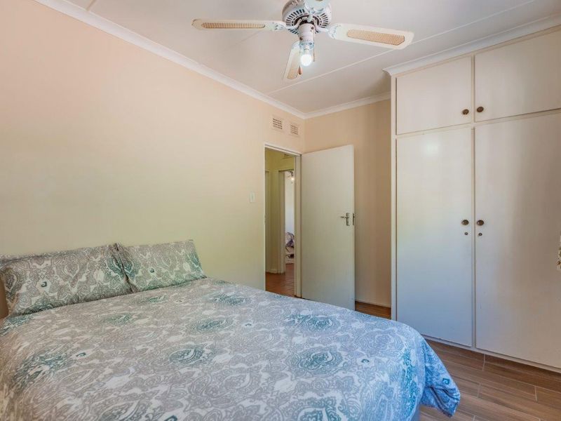 A functional bedroom featuring built-in cupboards, a ceiling fan, and tiled flooring, offering a neutral base for personalization.