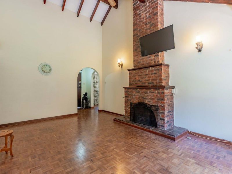 Spacious living room featuring a prominent brick fireplace, high vaulted ceilings with exposed timber beams, and classic parquet flooring.